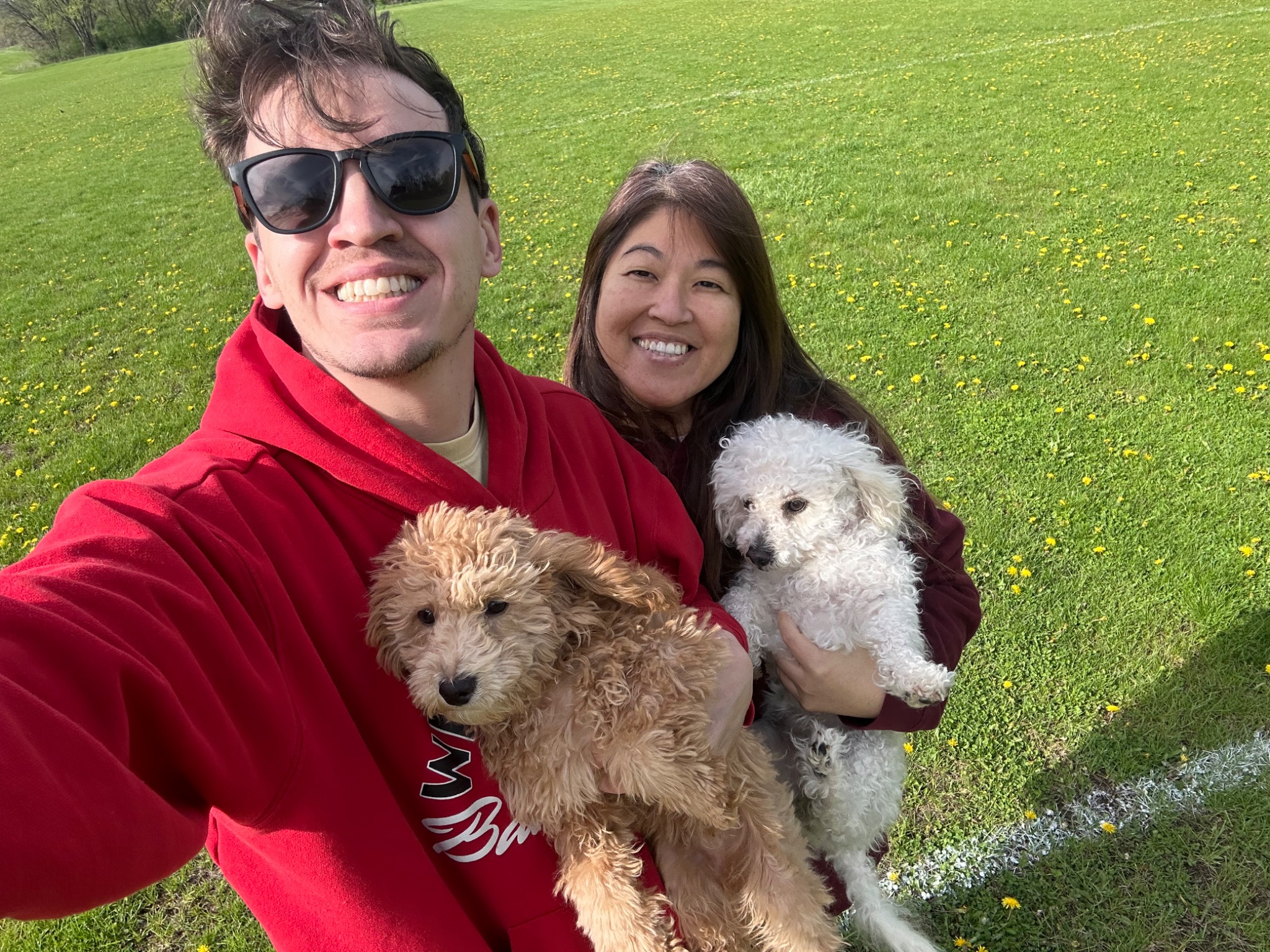 Ben and Jen smiling outdoors in a green field, each holding one of their two dogs.